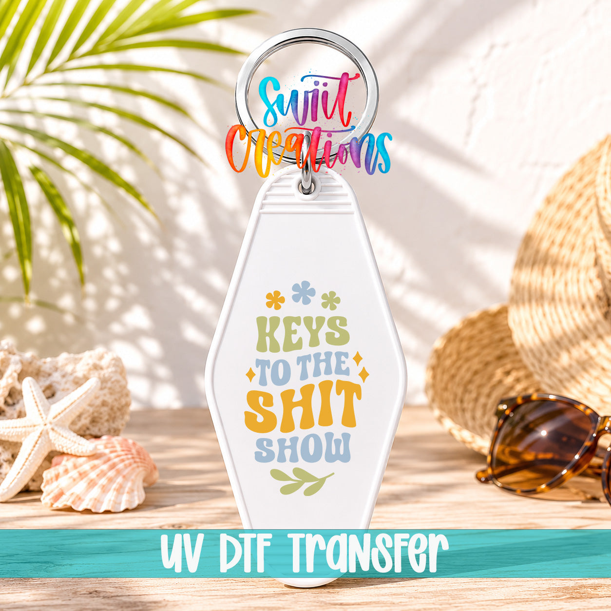 A keychain with a colorful design and text, placed on a wooden surface with sunglasses and a straw hat in the background.