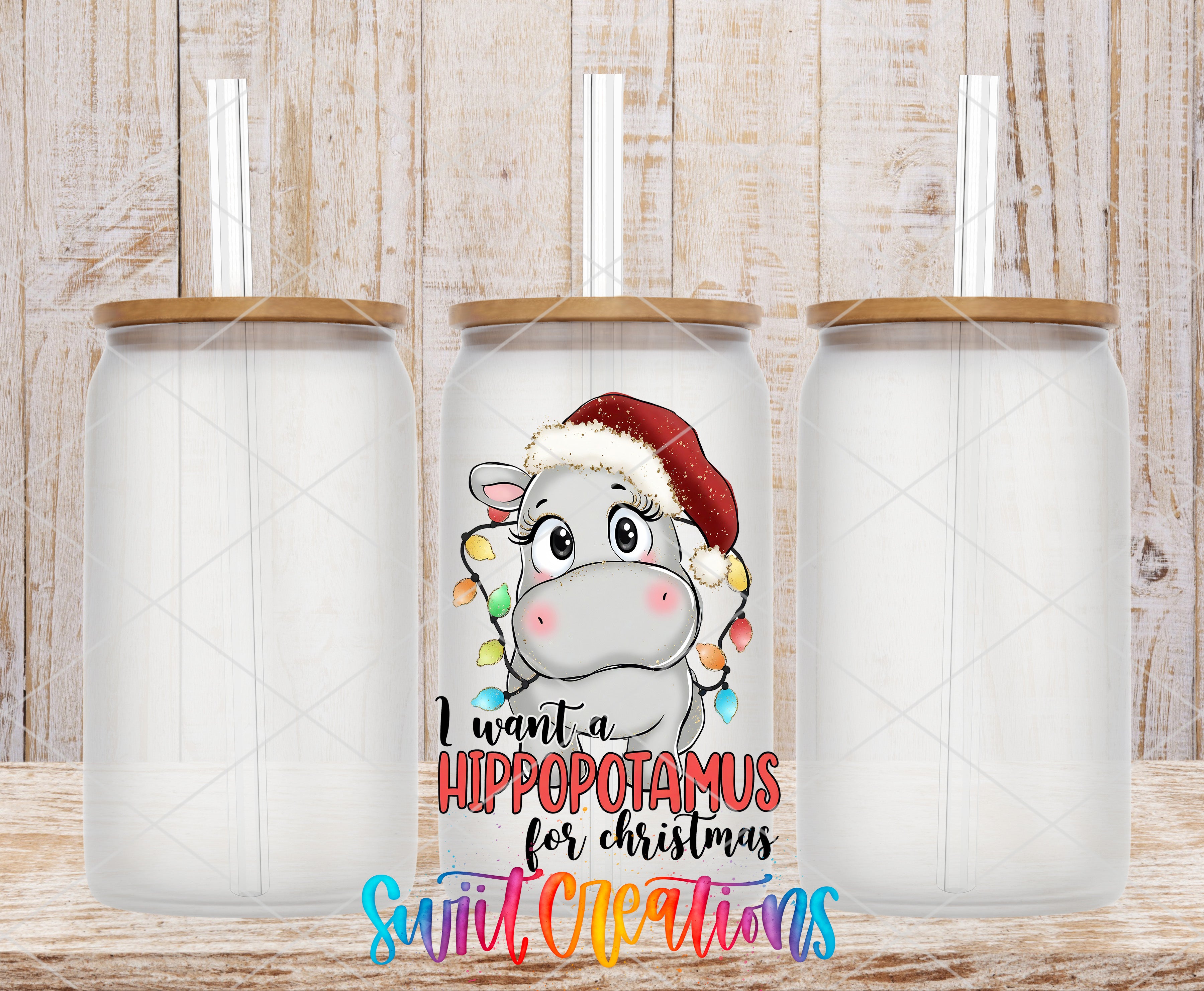 three clear glass jars with lids, each containing a straw. The jars are arranged in a row, with the middle jar having a printed design of a cartoon hippopotamus wearing a Santa hat. The text on the jars reads "I want a Hippopotamus for Christmas" and "Swift Creations".