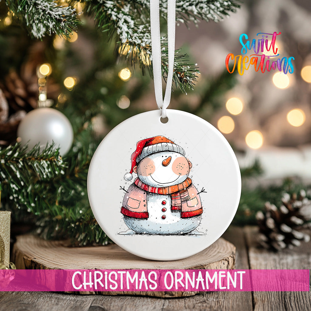 A white Christmas ornament featuring a snowman is hanging from a ribbon, with a blurred background of a decorated Christmas tree and other ornaments.