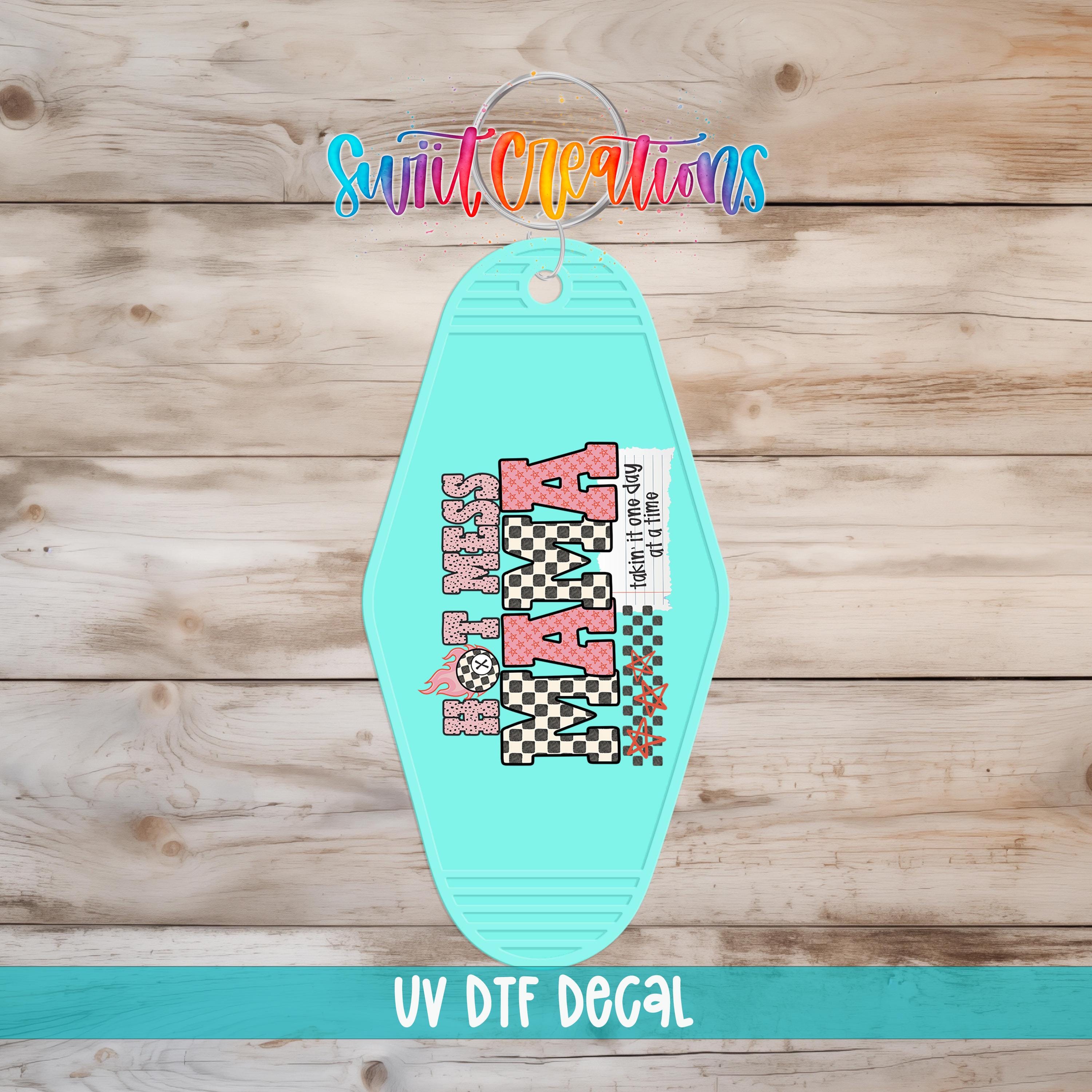 A turquoise keychain with a checkered pattern and the word "KARA" printed on it, placed on a wooden surface.