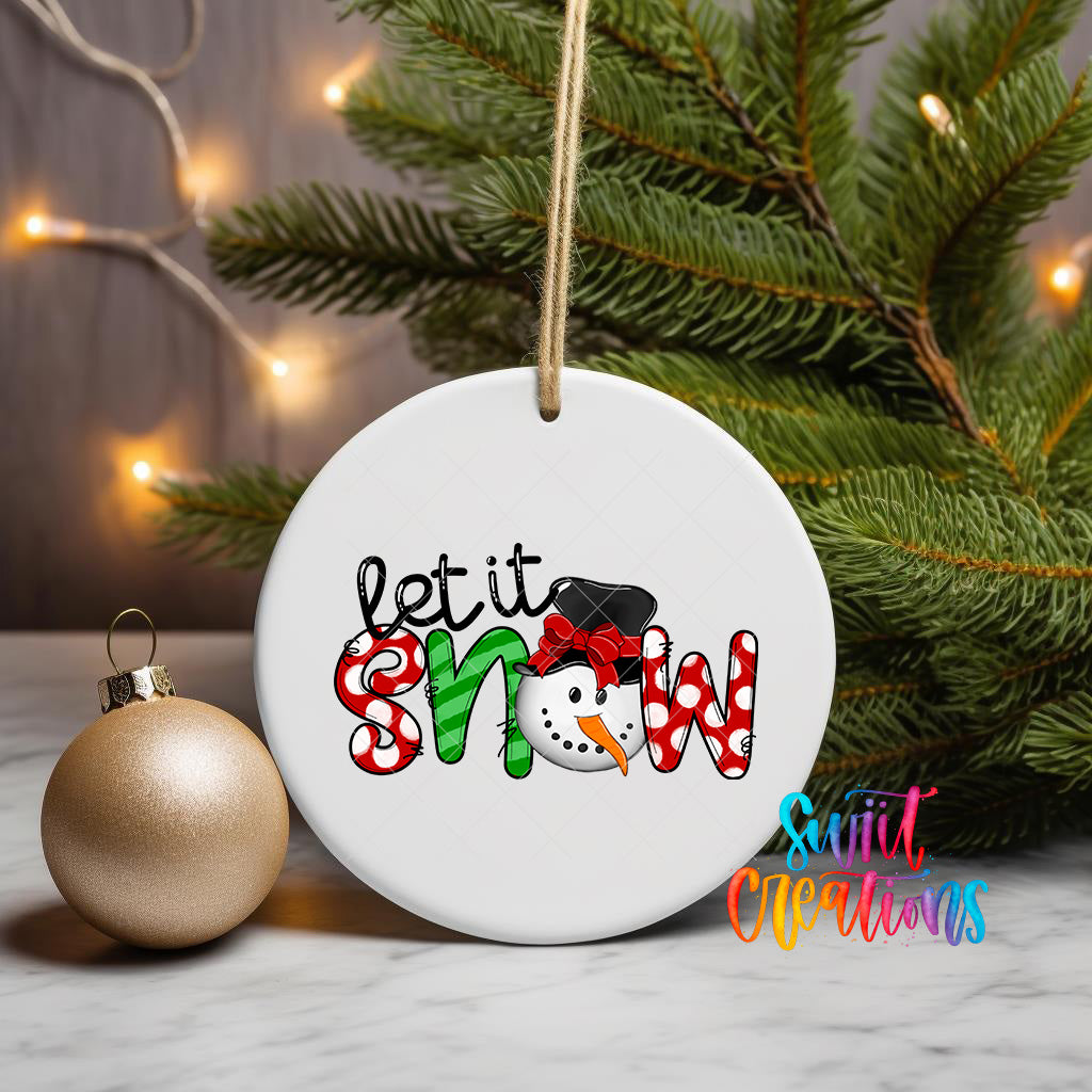 A white ornament with the text "let it snow" and a snowman graphic is displayed on a table, with a gold ornament and a Christmas tree in the background.