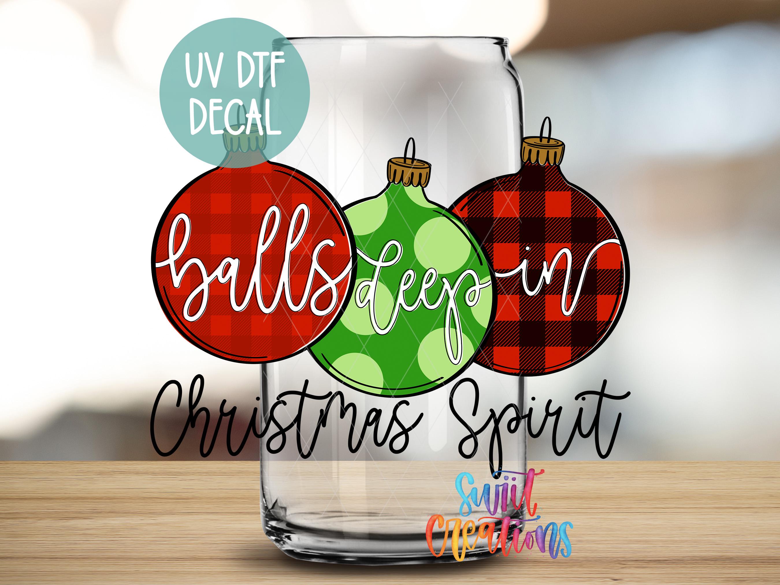A glass with three Christmas ornaments, each with a different color and pattern, along with the text "balls deep" and "Christmas Spirit" written on it.