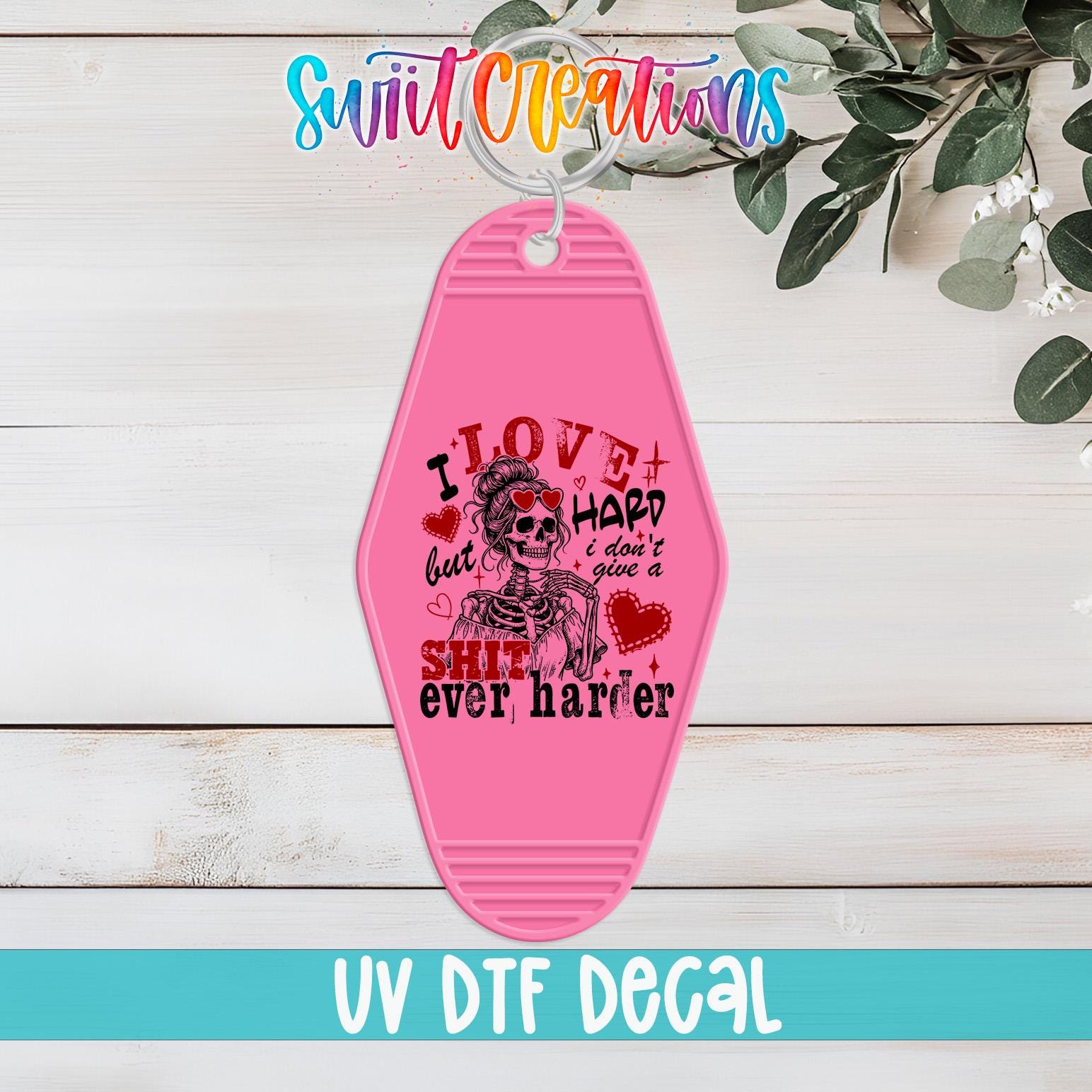 A pink keychain with a skull and skeleton design, along with text that says "I LOVE but I HARD don't give a SHIT ever harder".