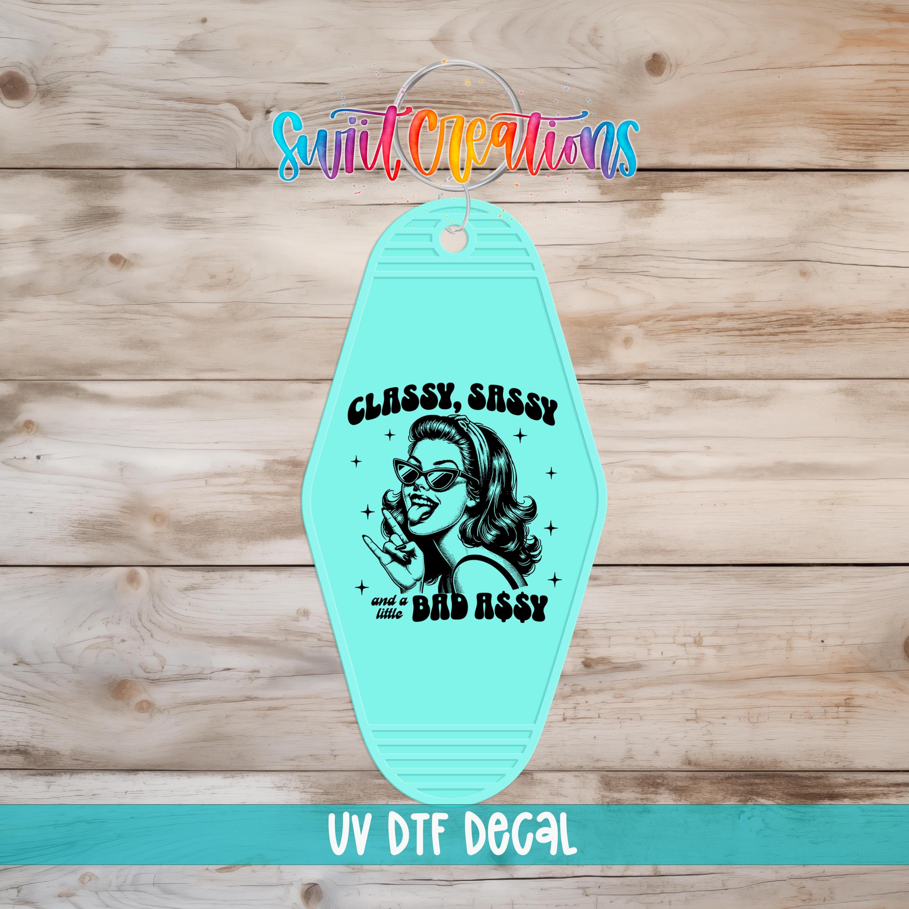 A turquoise keychain with a graphic design featuring a woman's face and the text "CLASSY SASSY and a little BAD ASSY" printed on it.