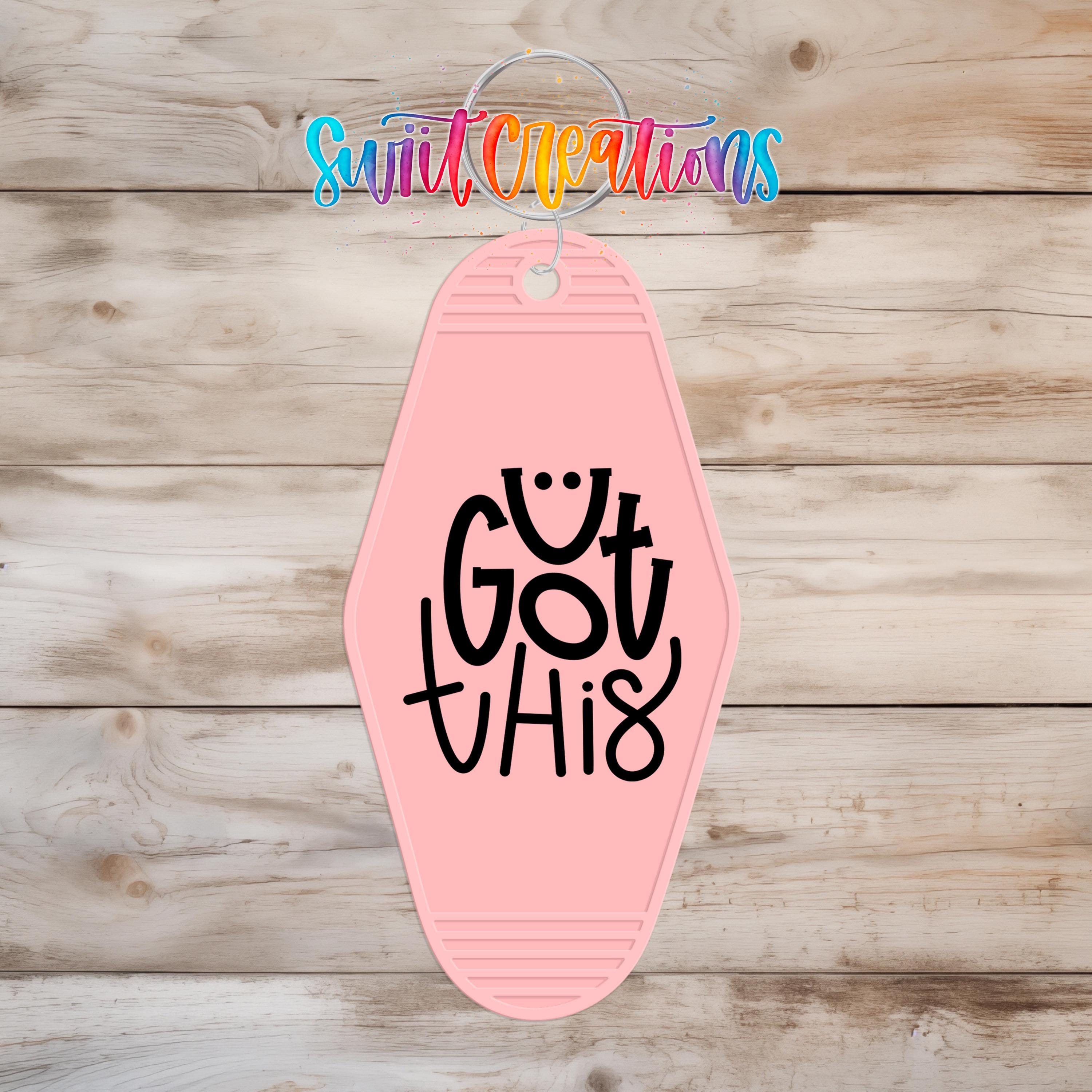 A pink keychain with the text "Got this" printed on it, hanging on a wooden surface.