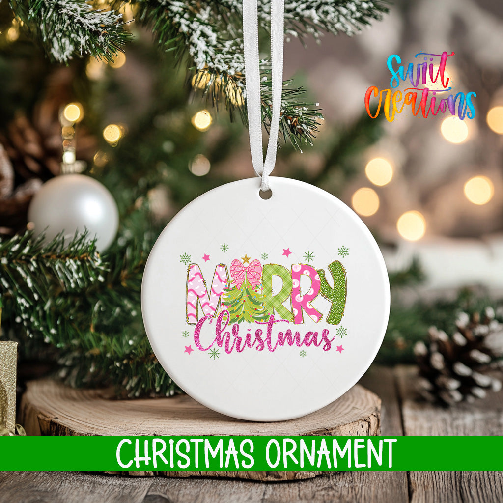 A white Christmas ornament with the text "Merry Christmas" in pink and green colors, hanging on a tree branch.