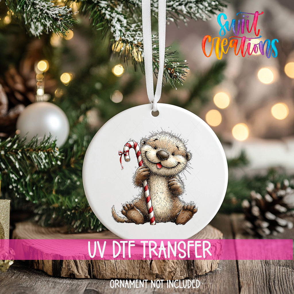 A white ornament with a cute otter holding a candy cane is hanging on a Christmas tree.