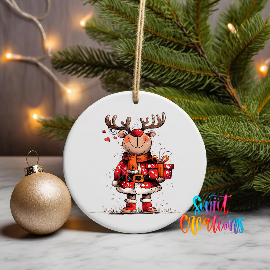 A white ceramic ornament featuring a cartoon reindeer holding a gift box, surrounded by Christmas lights and greenery.
