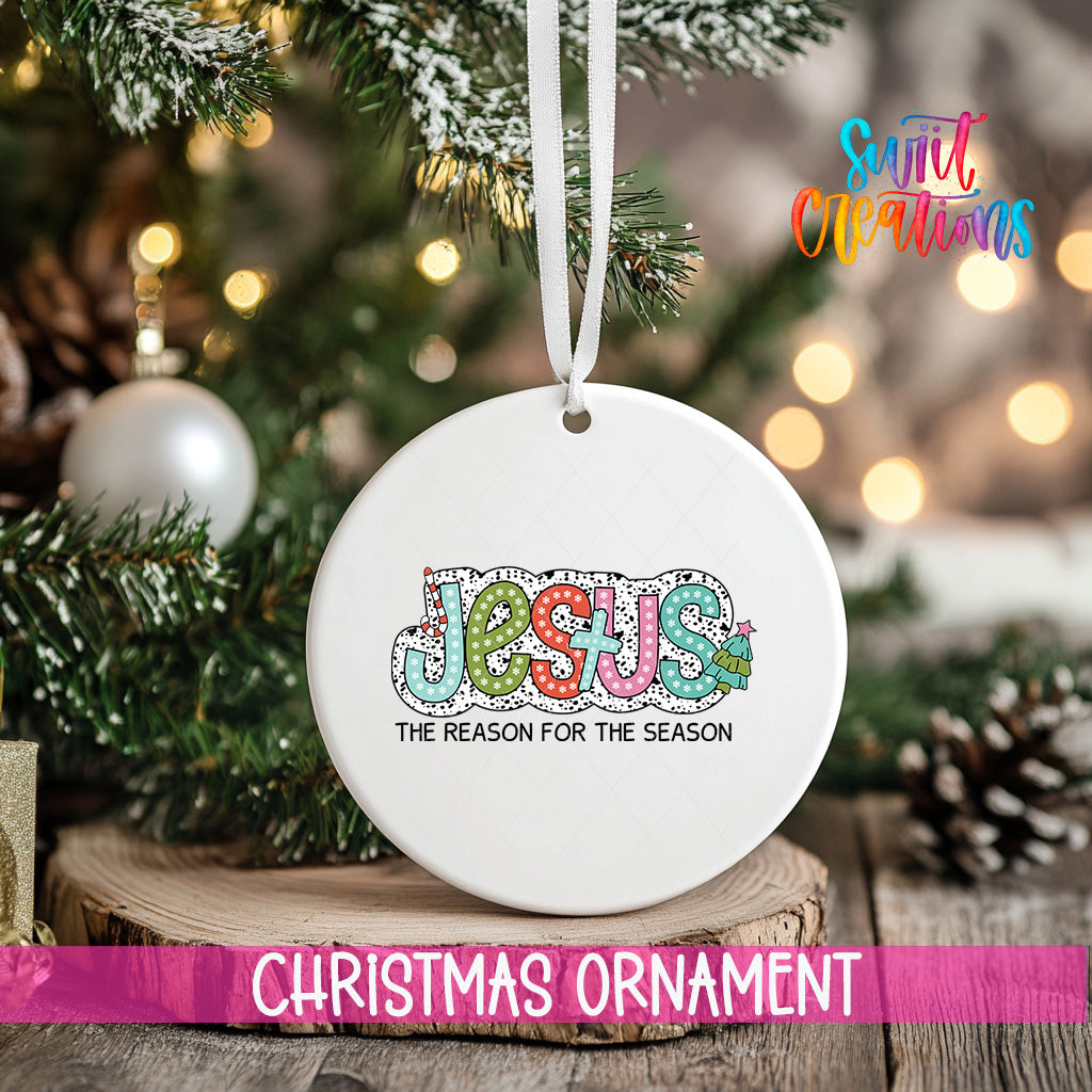 A white Christmas ornament with the word "JESUS" written on it, hanging from a tree branch.