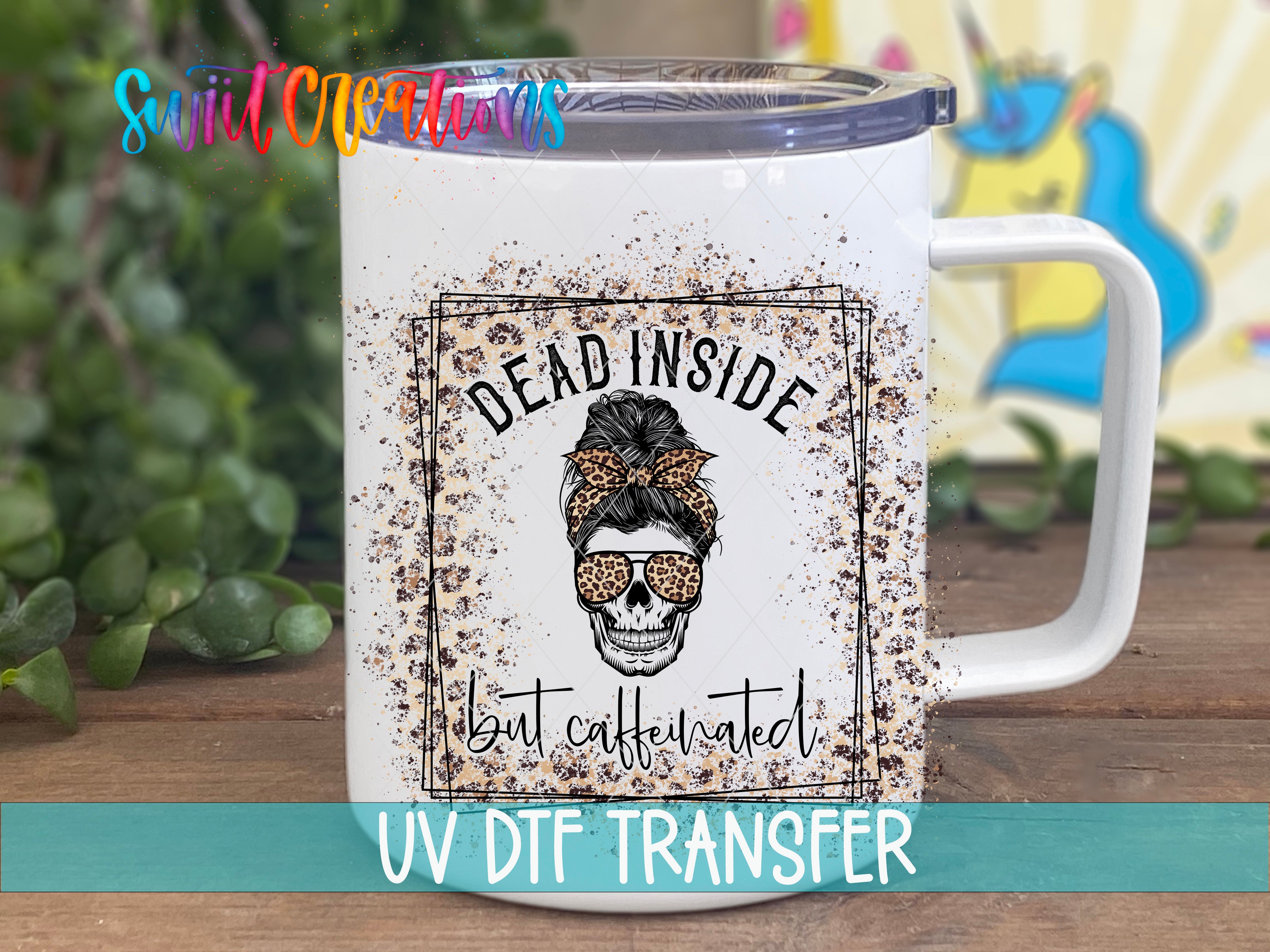 A white mug with a black and white skull design and the text "Dead inside but caffeinated" printed on it, along with a UVDF (ultraviolet dye-free transfer) logo.