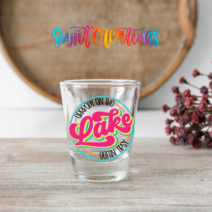 Everybody on the Lake Gettin Tipsy shot glass transfer on a clear glass beside a wooden barrel and dried flowers