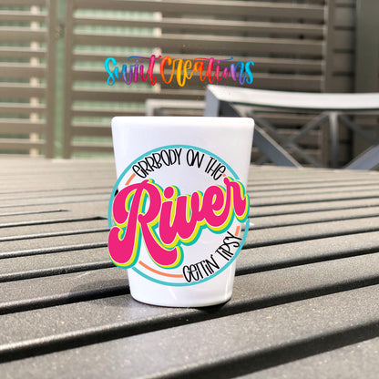 Everybody on the River Gettin Tipsy UV DTF transfer on a white shot glass on an outdoor patio table