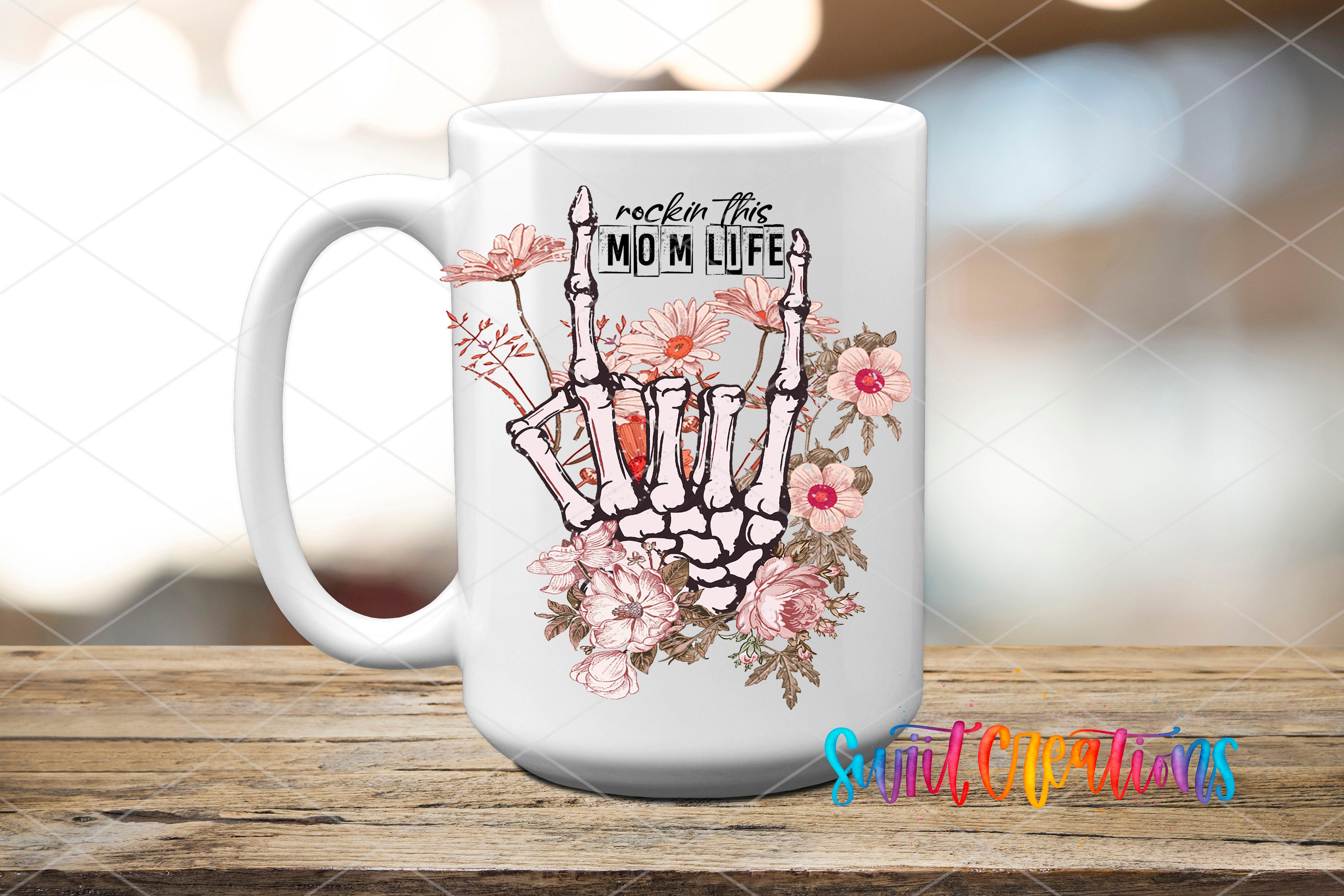A white ceramic mug with a floral design and the text "rockin this MOM LIFE" printed on it, placed on a wooden surface.
