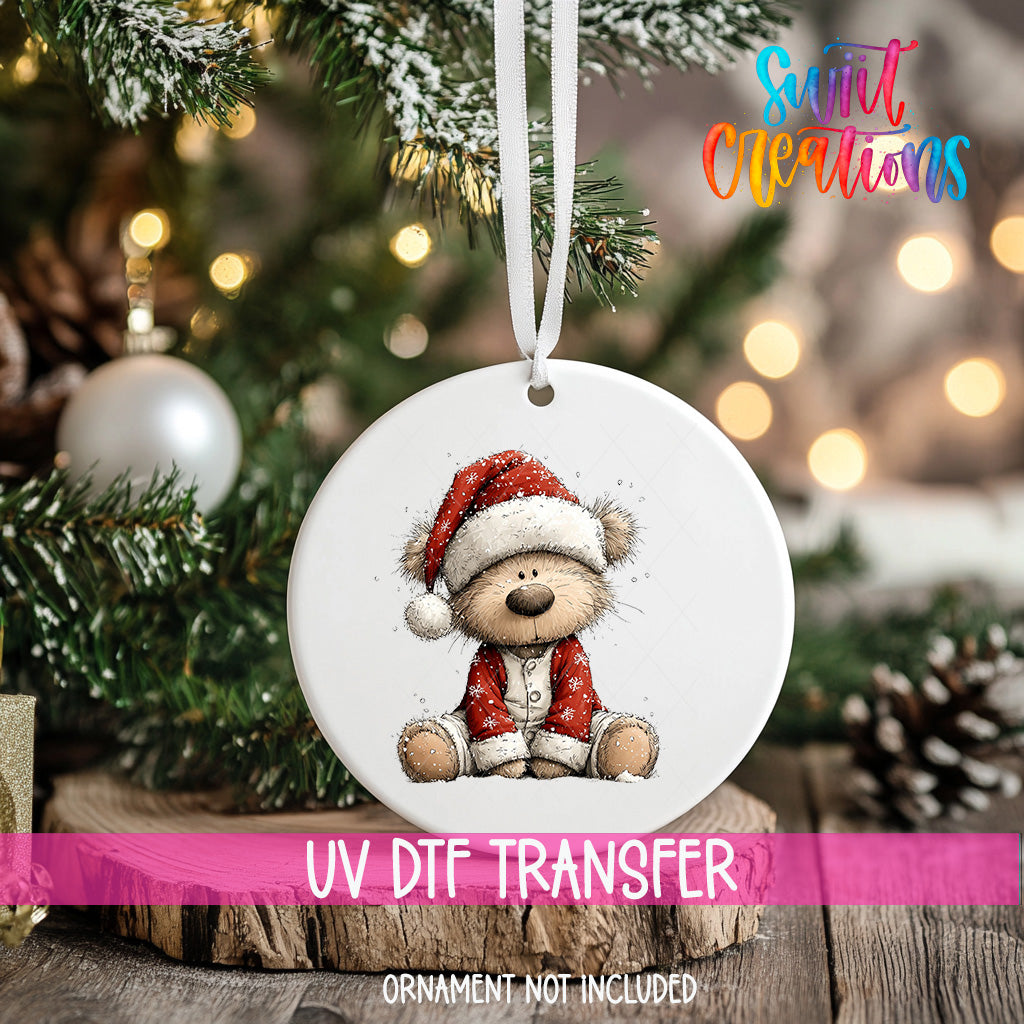 A white Christmas ornament with a teddy bear wearing a Santa hat is hanging on a tree.