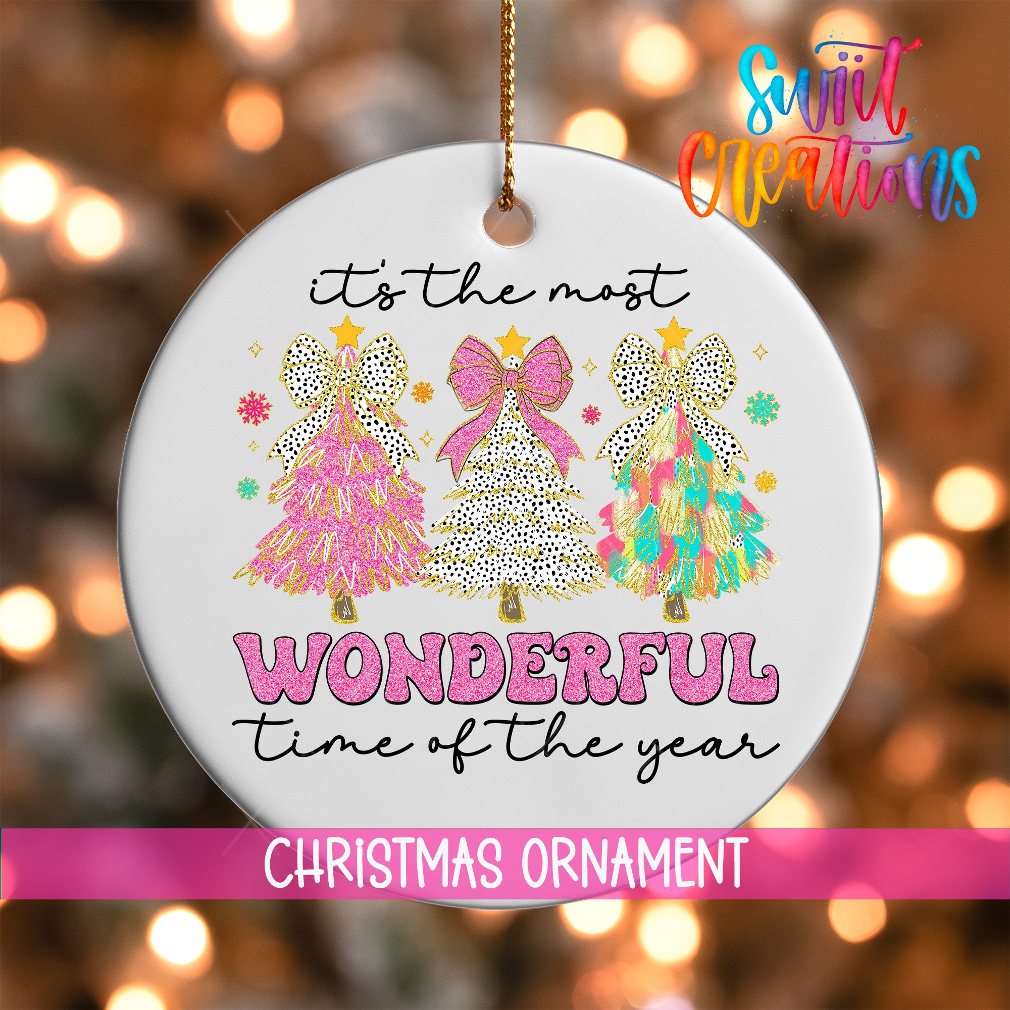 A white Christmas ornament with a festive design featuring three colorful Christmas trees and the text "It's the most wonderful time of the year" in a pink and white color scheme.