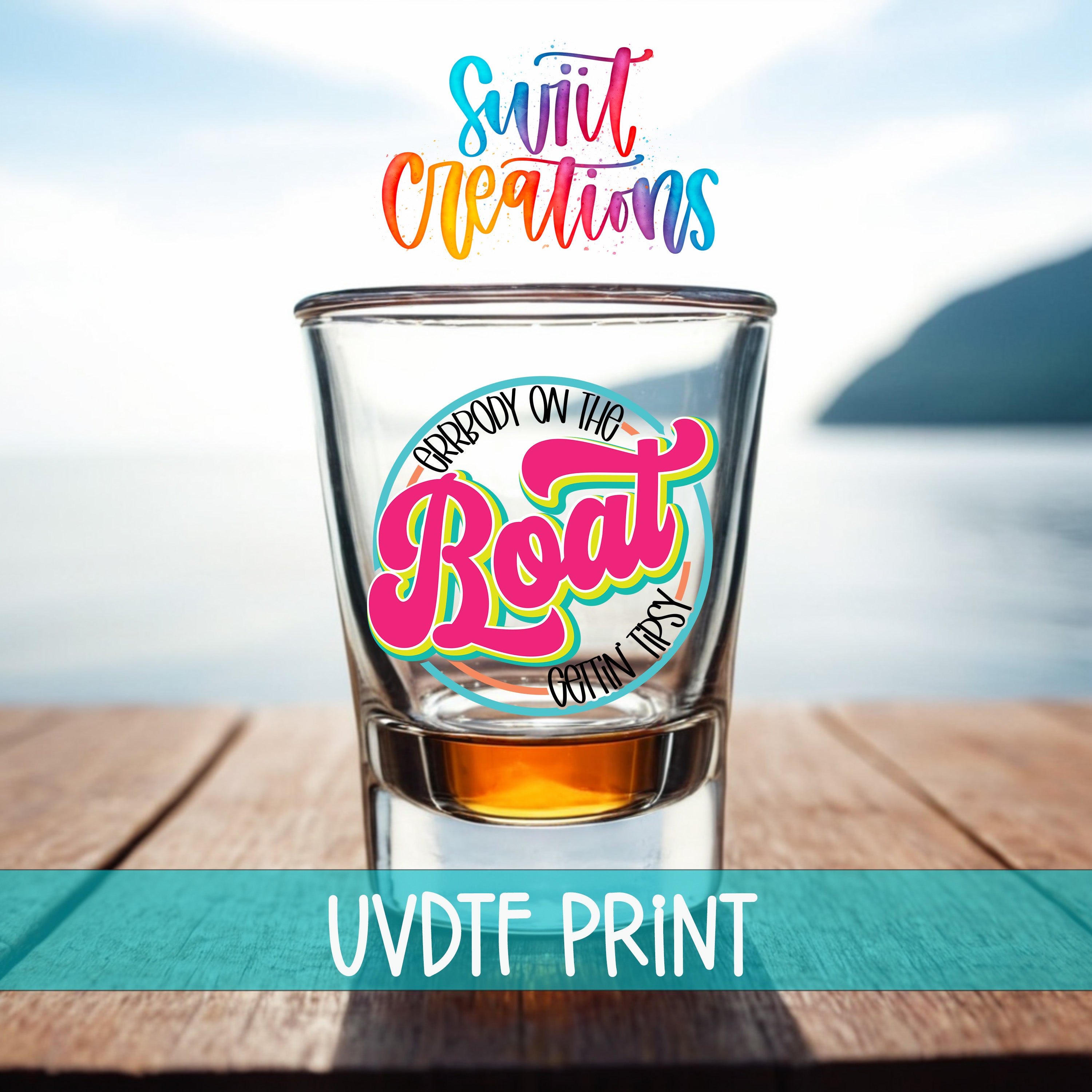A shot glass with a colorful design on it, placed on a wooden surface with a body of water in the background.
