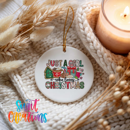 A white ceramic ornament with a colorful design hangs on a white knitted blanket, surrounded by dried wheat and a lit candle.
