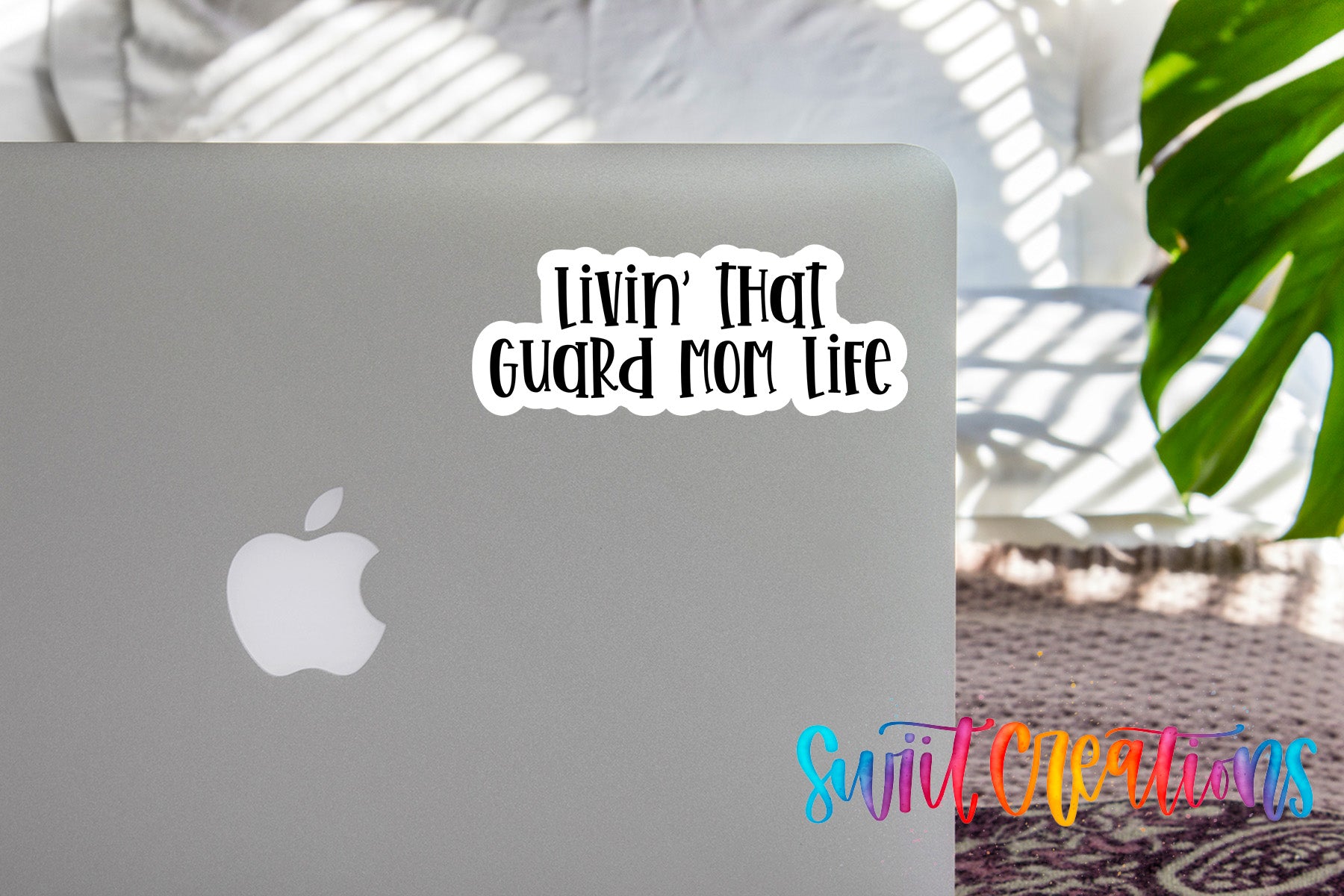 a sticker with the text "LIVIN' THAT GUARD MOM LIFE" on the back of a silver Apple laptop.