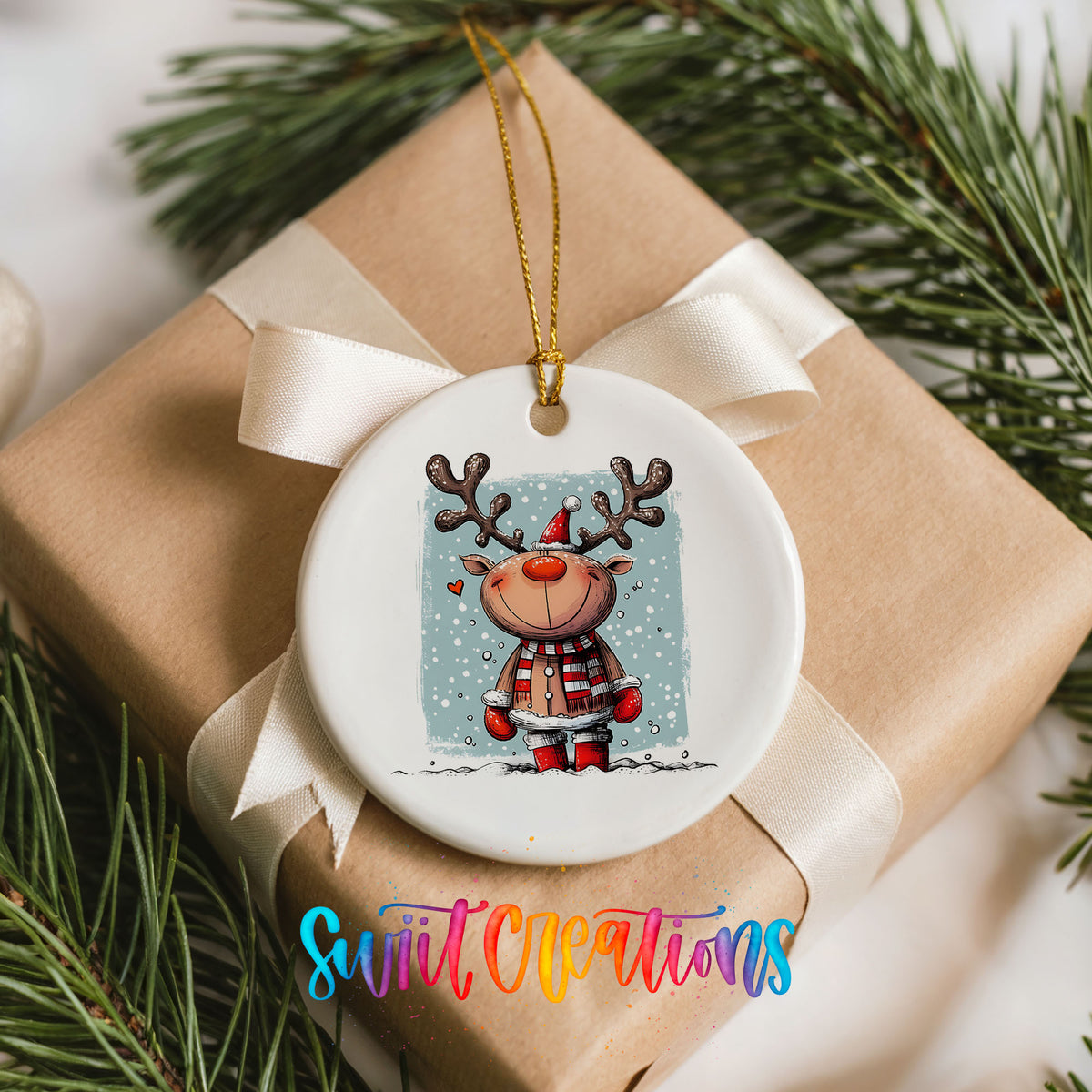 A white ceramic ornament with a reindeer design hangs on a brown gift box, surrounded by pine branches.