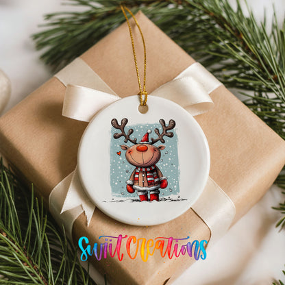 A white ceramic ornament with a reindeer design hangs on a brown gift box, surrounded by pine branches.