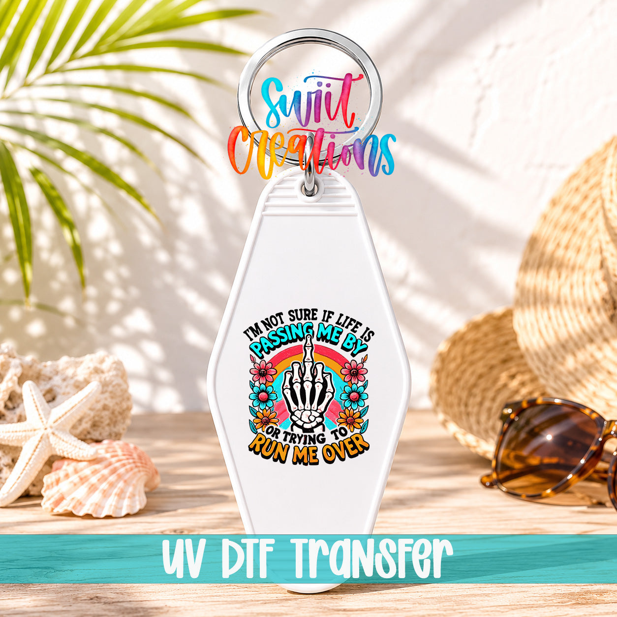 A keychain with a colorful design and text, placed on a wooden surface with sunglasses and a straw hat in the background.