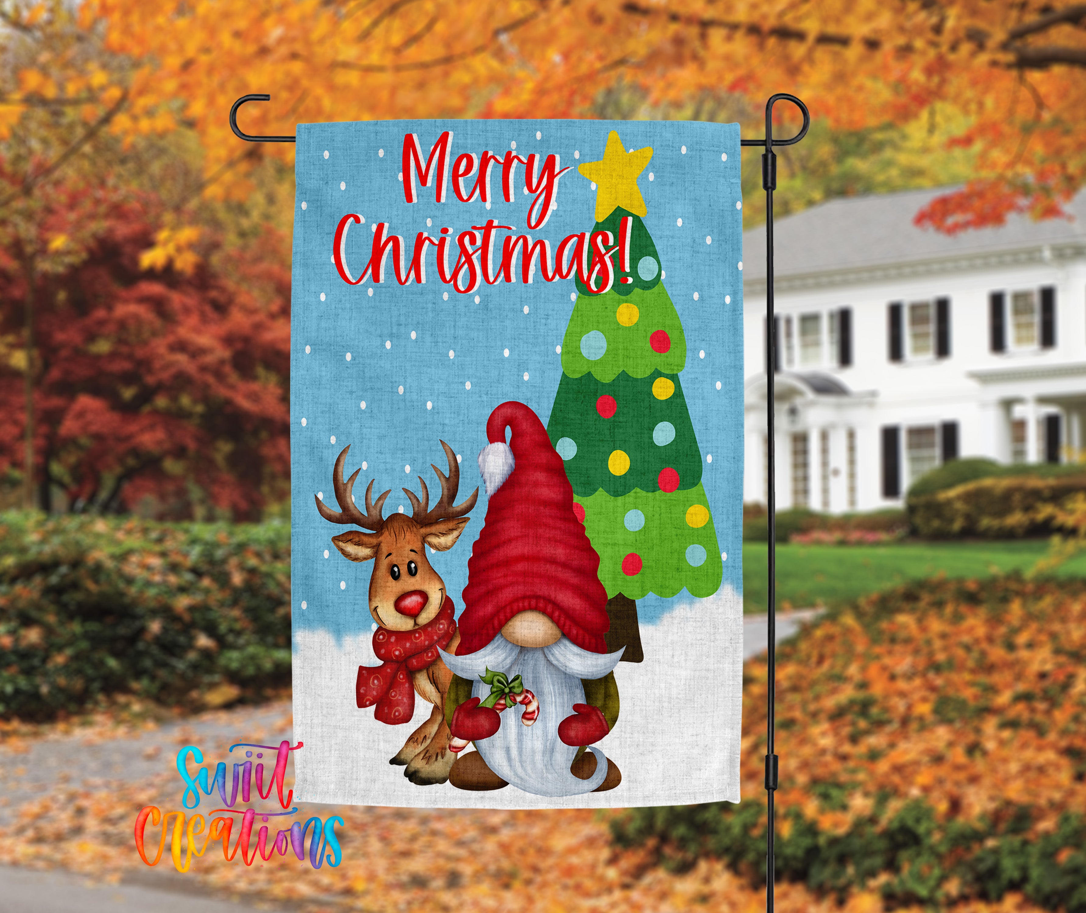 A colorful Christmas-themed flag with a gnome and a reindeer, set against a backdrop of a white house and autumn foliage.