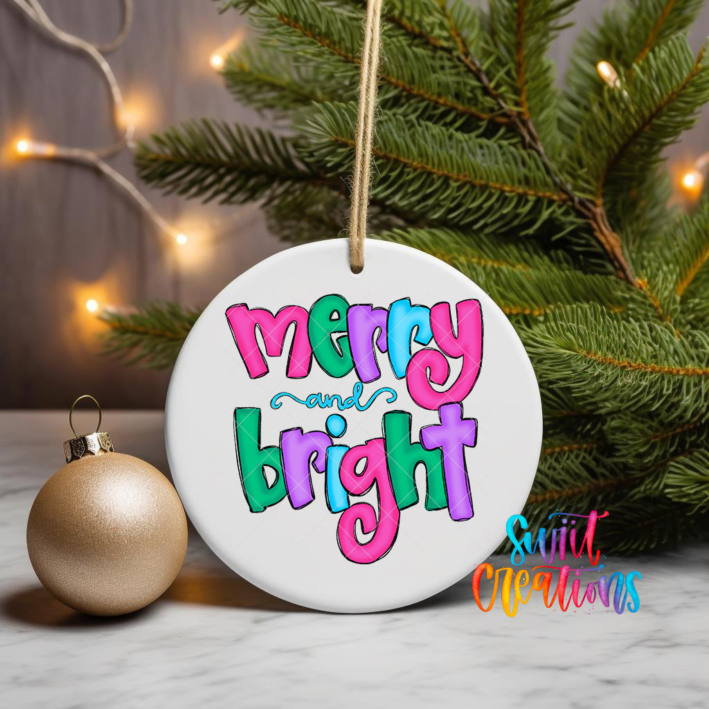 A white ceramic ornament with the text "merry and bright" in colorful letters is displayed on a white marble surface, with a gold ornament and a pine tree in the background.