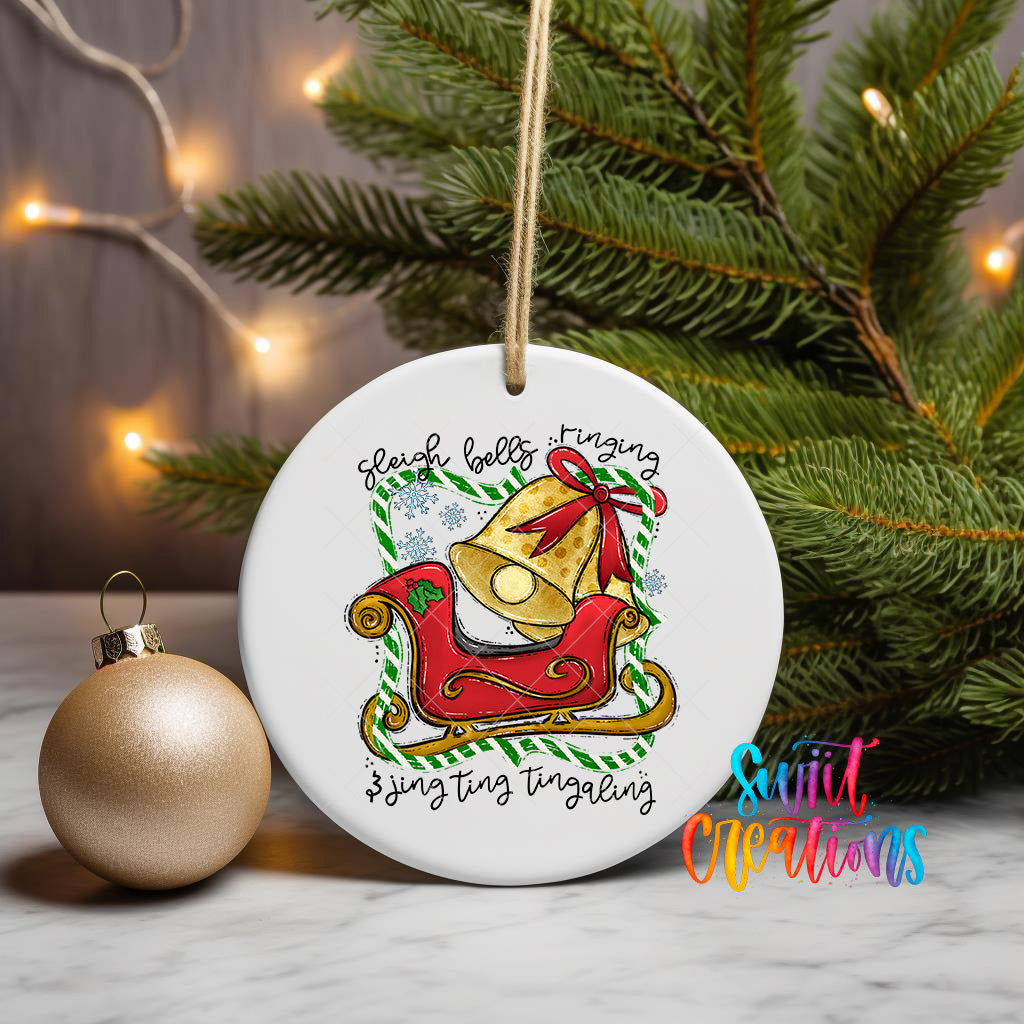 A white ceramic ornament with a Christmas tree in the background, featuring a bell and the text "Sleigh bells ringing" and "singing singing singing".