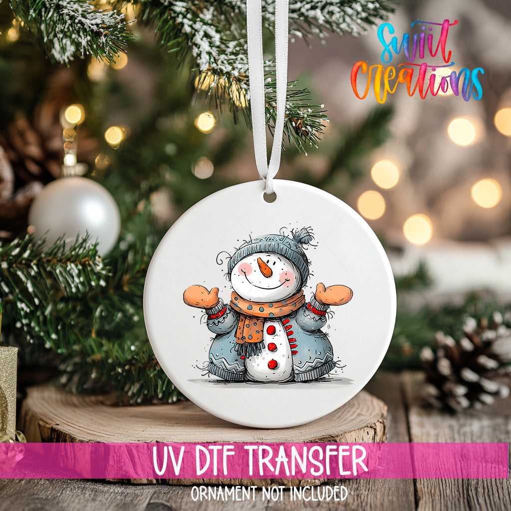 A white ornament with a snowman design hangs on a Christmas tree, surrounded by pine branches and twinkling lights.