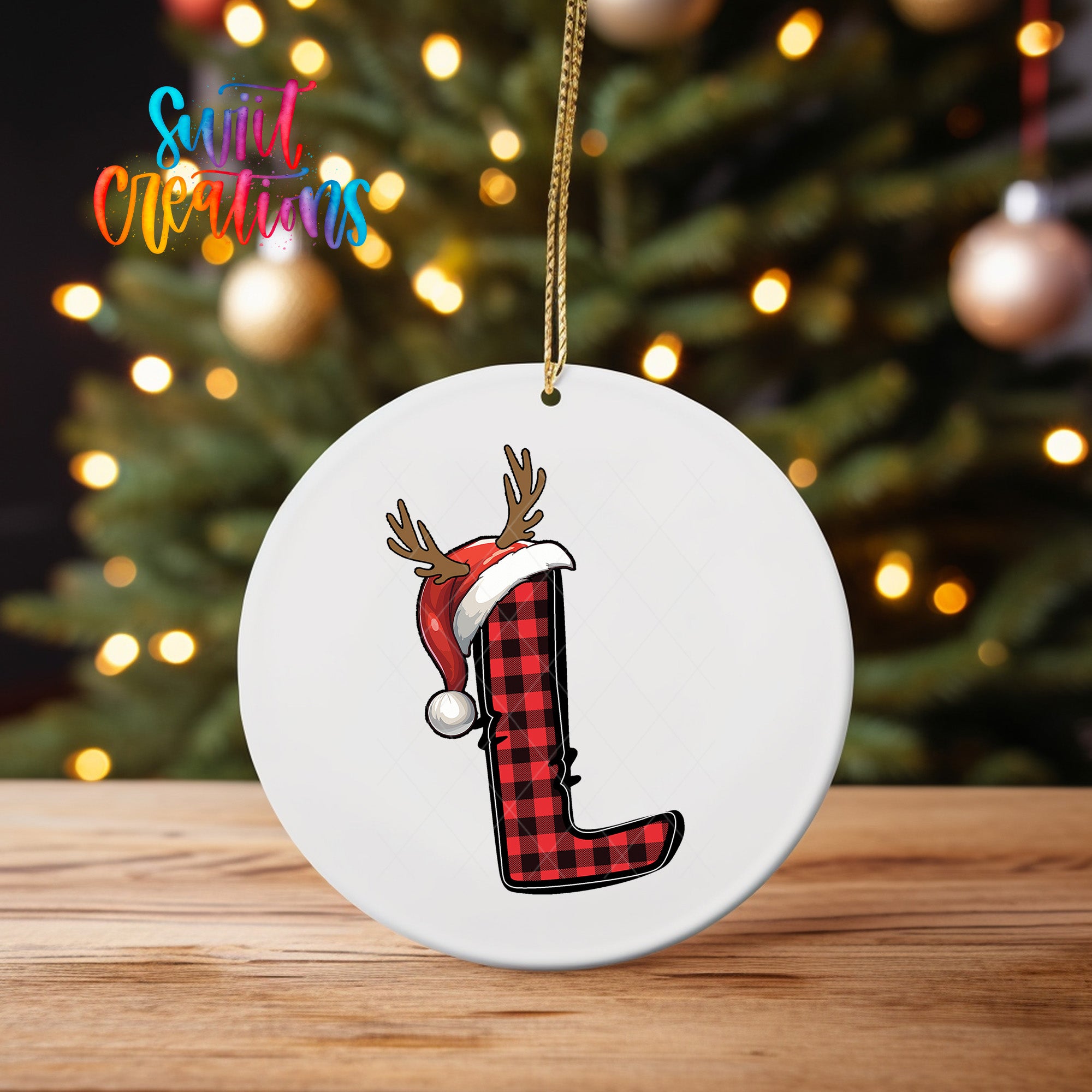 A white ornament with a red and black plaid reindeer hat and the letter "L" on it, hanging on a string.