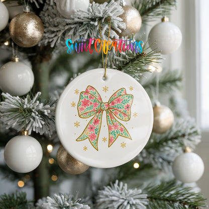 A white ceramic ornament with a floral design and a bow is hanging on a Christmas tree, surrounded by white and gold ornaments.