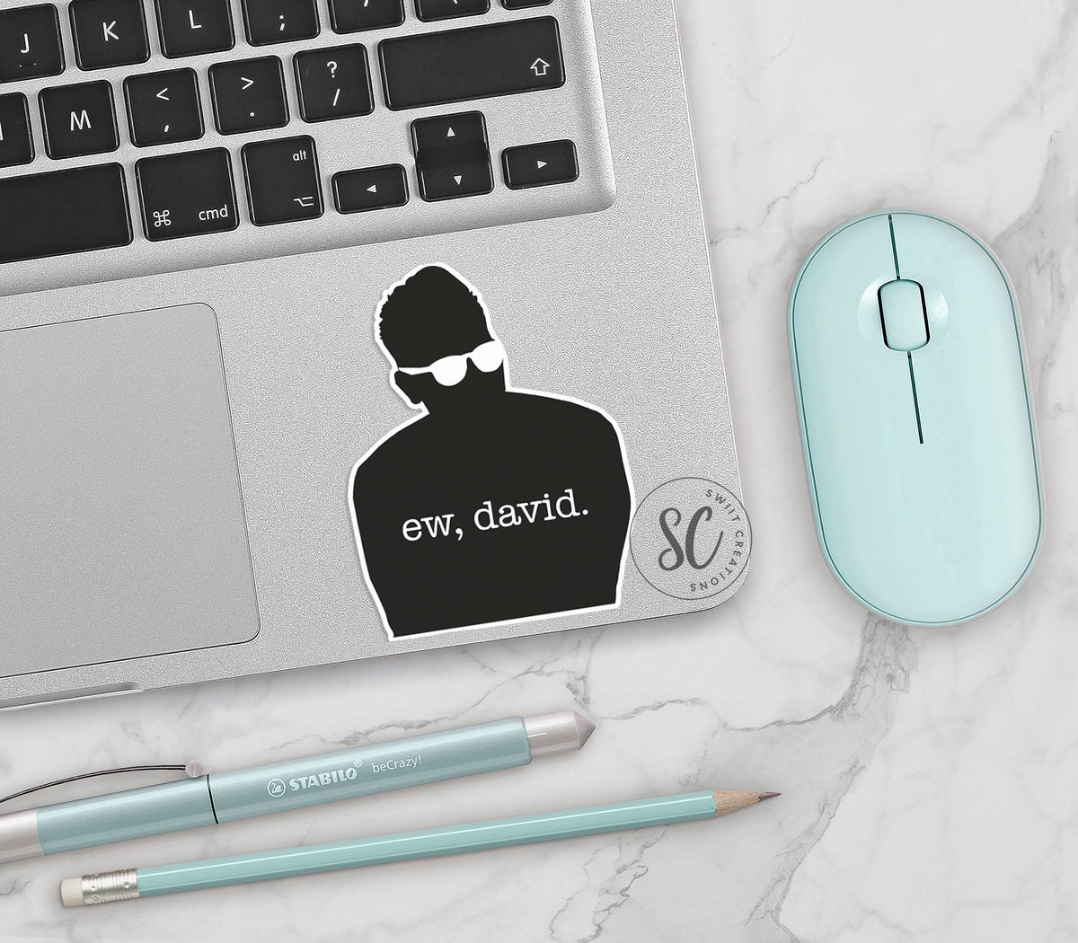 Ew David Silhouette vinyl sticker on a silver laptop next to a mint mouse and pens