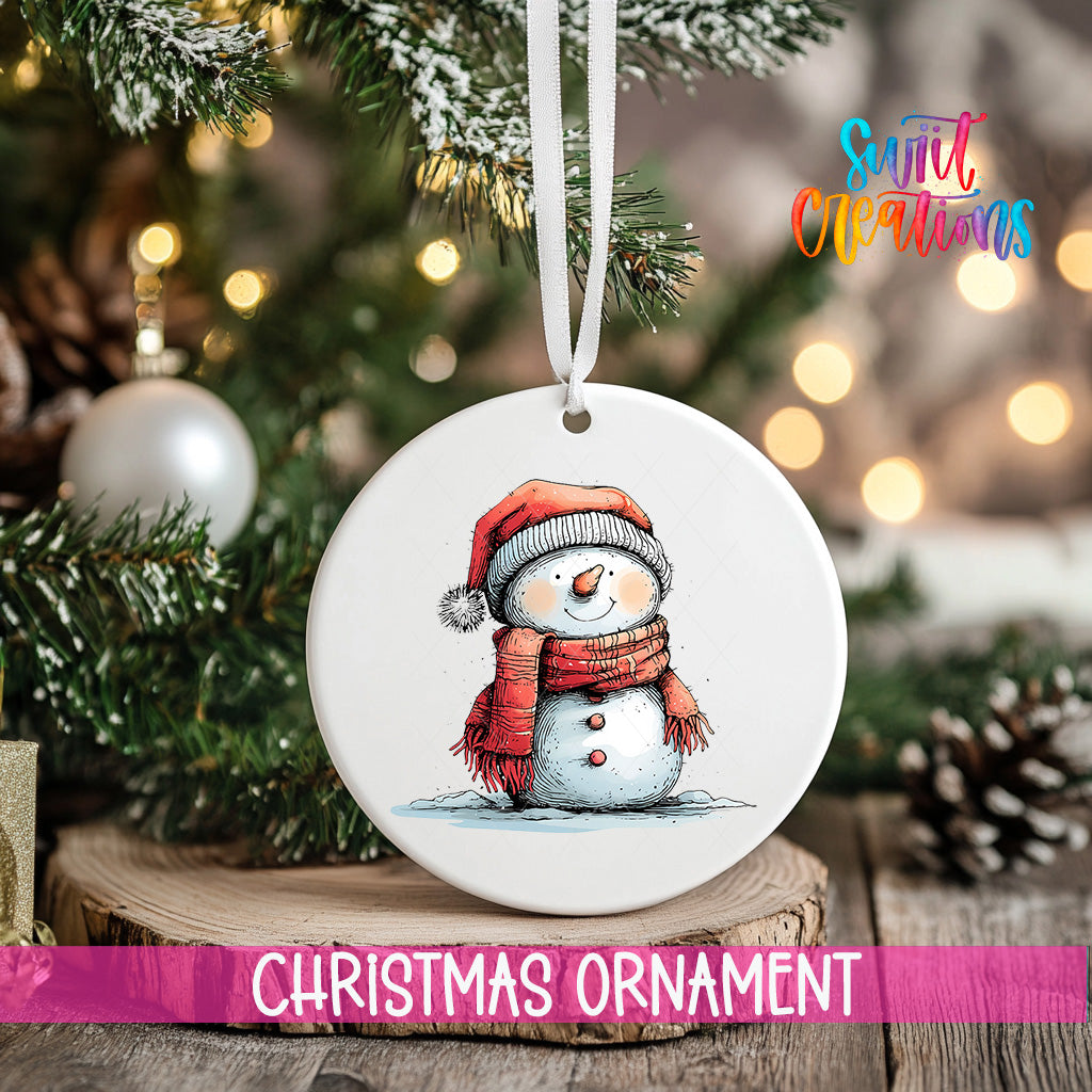 A white Christmas ornament featuring a snowman is hanging from a ribbon, with a blurred background of a decorated Christmas tree and other ornaments.