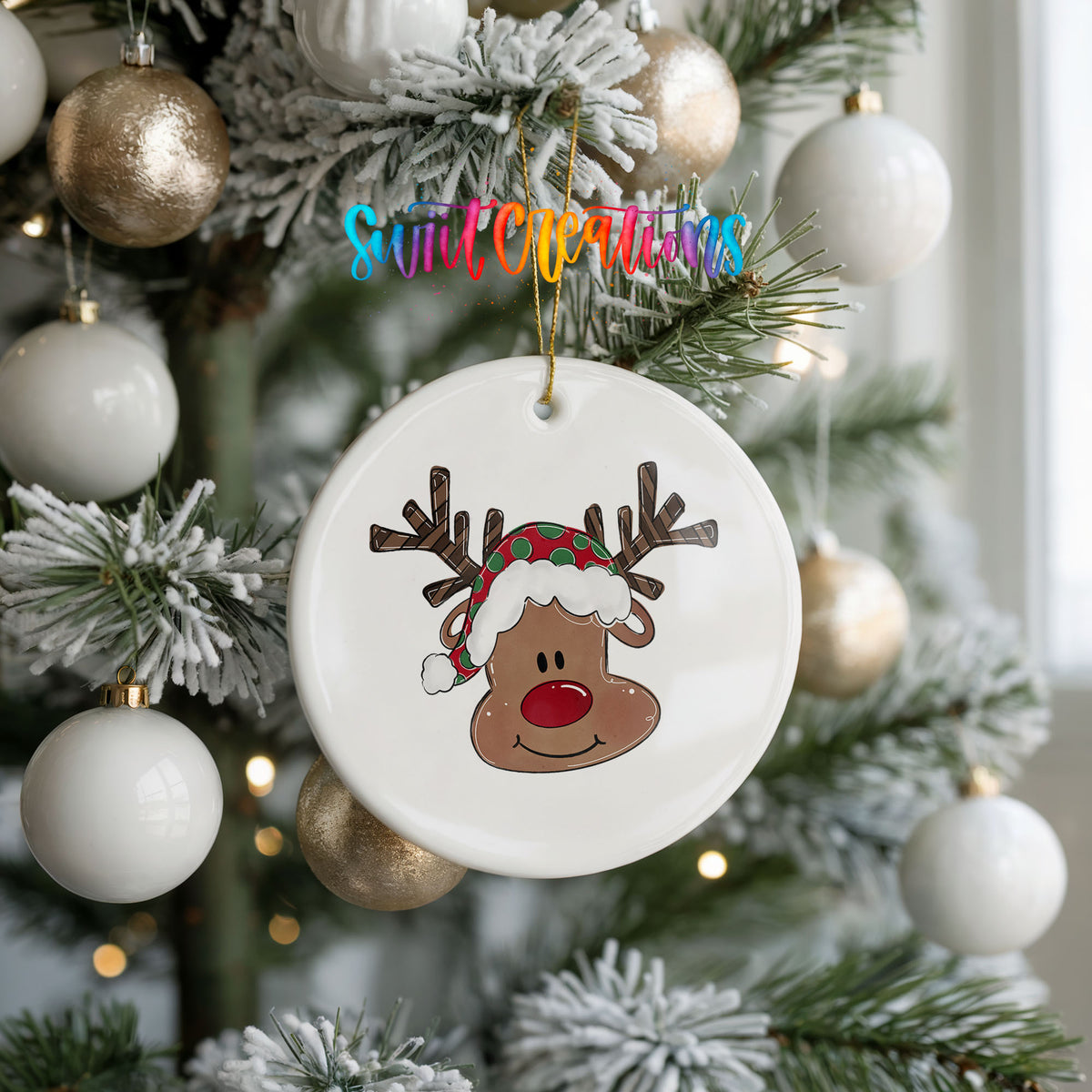 A white ceramic ornament with a cartoon reindeer wearing a Santa hat is hanging on a Christmas tree.