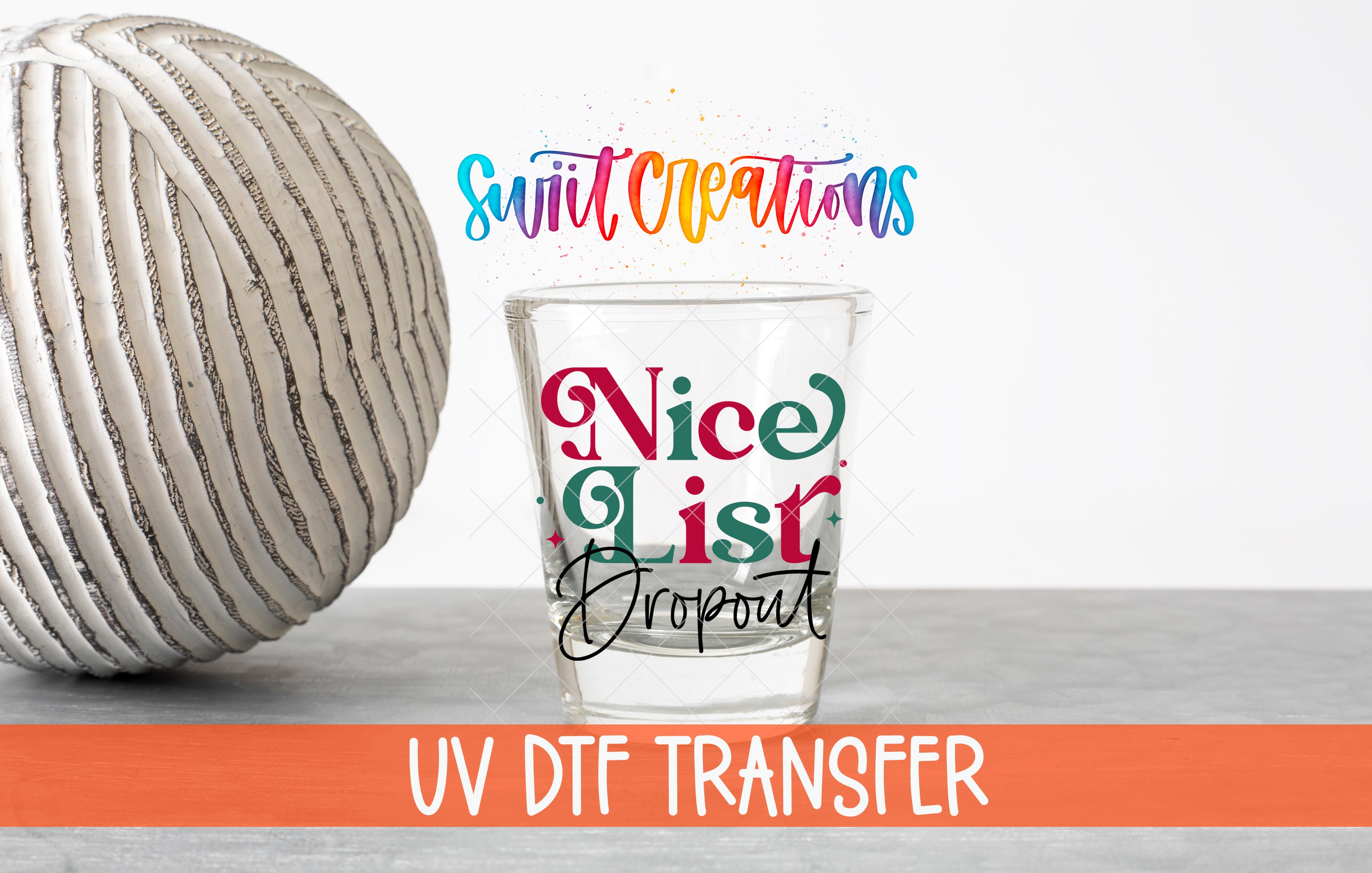 a glass with a colorful design and text, placed next to a white ball on a gray surface.