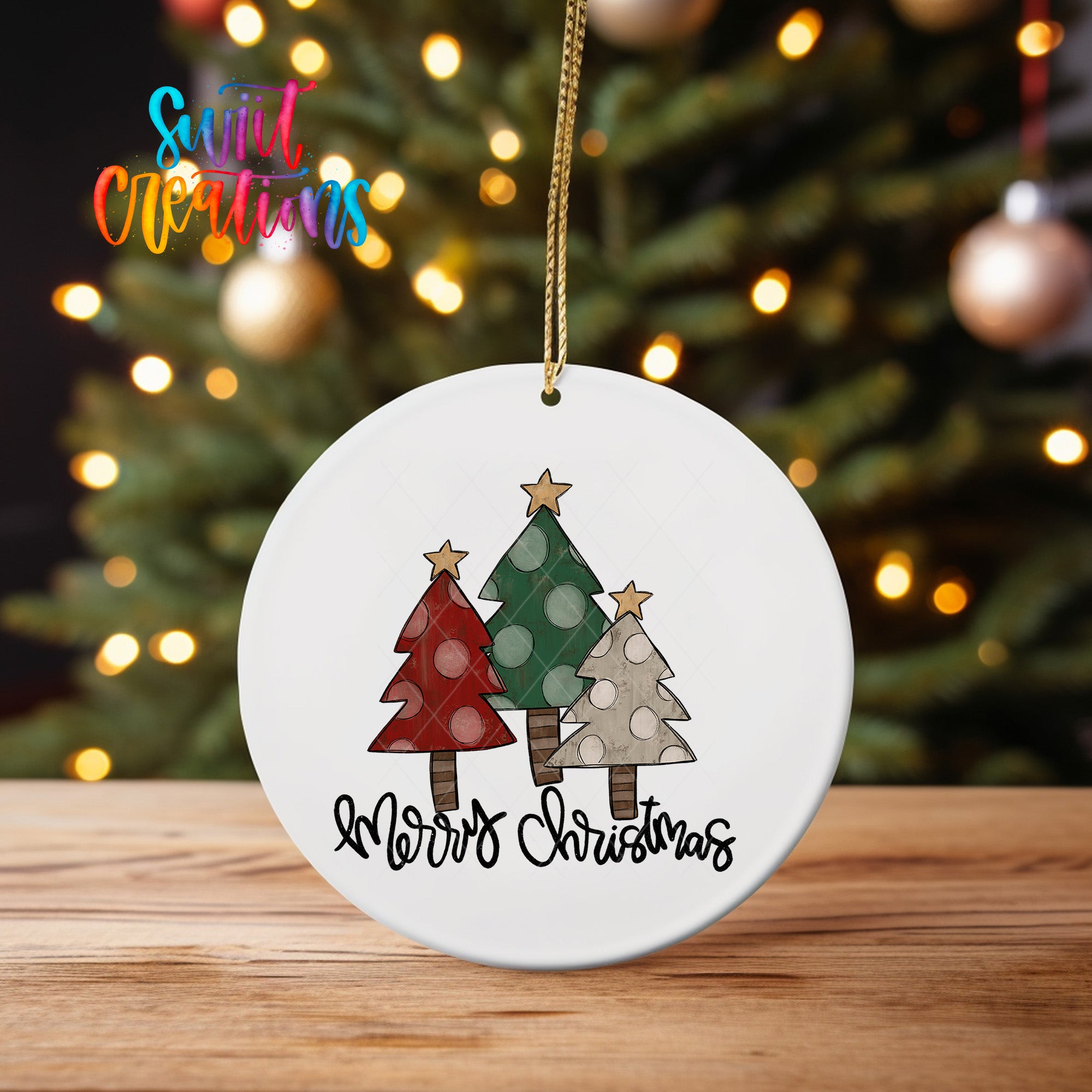 A white Christmas ornament with a design of three trees, each with a different color and pattern, hangs on a string. The ornament has the text "Merry Christmas" written on it.