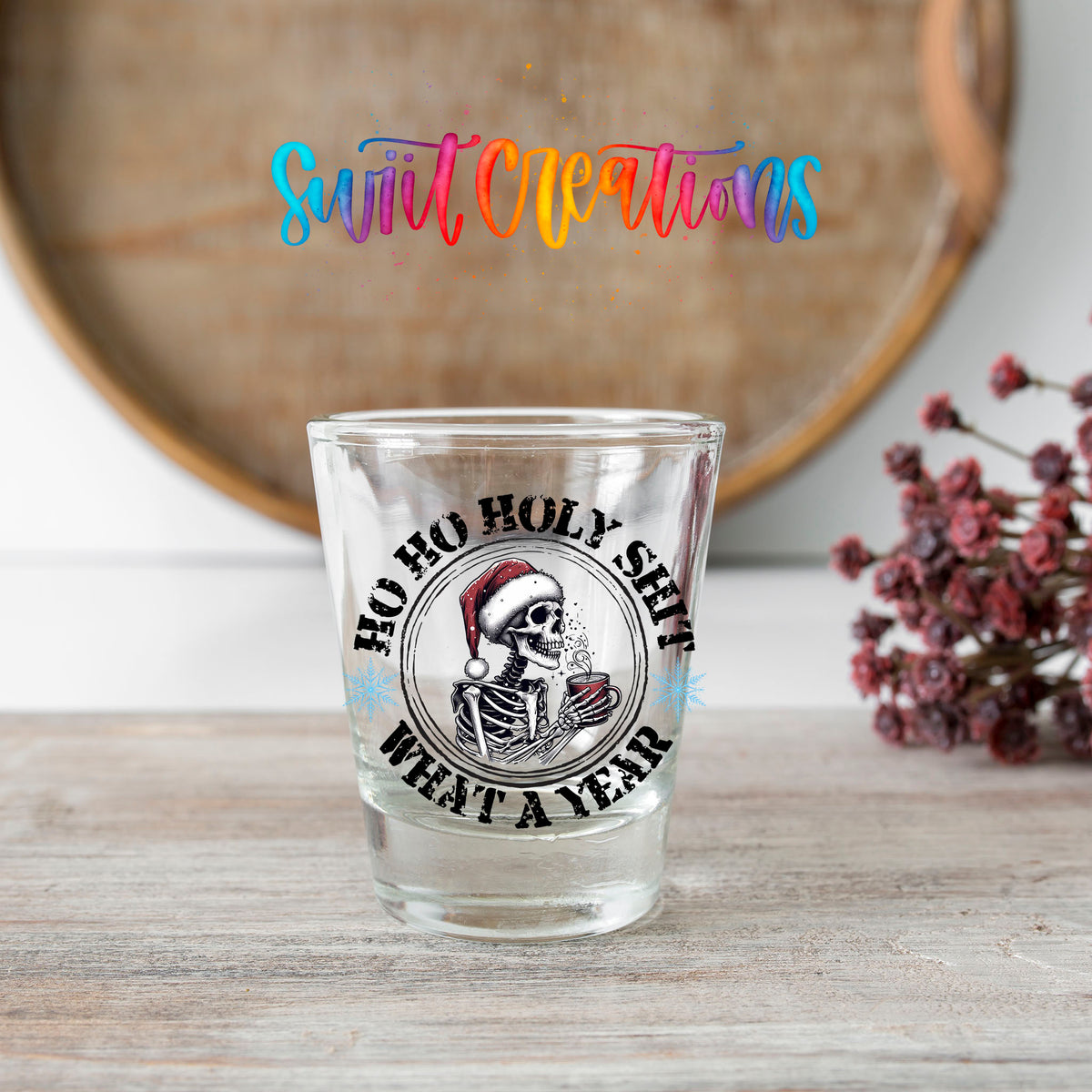 Ho Ho Holy Sh*t What a Year shot glass transfer on a clear glass beside a wooden barrel and dried flowers