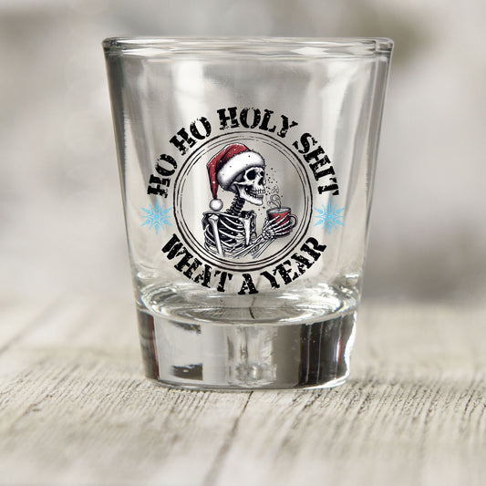 Ho Ho Holy Sh*t What a Year shot glass UV DTF transfer with skeleton in a Santa hat with a red mug on a clear shot glass