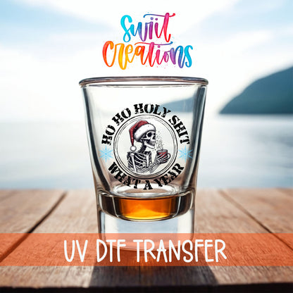 Ho Ho Holy Sh*t What a Year shot glass UV DTF transfer on a filled shot glass on a dock by the water