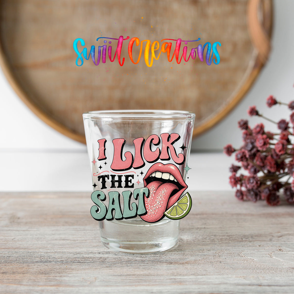 I Lick The Salt shot glass transfer on a clear glass beside a wooden barrel and dried flowers