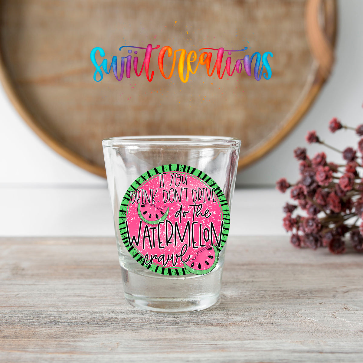If You Drink Don't Drive Watermelon Crawl shot glass transfer on a clear glass beside a wooden barrel and dried flowers