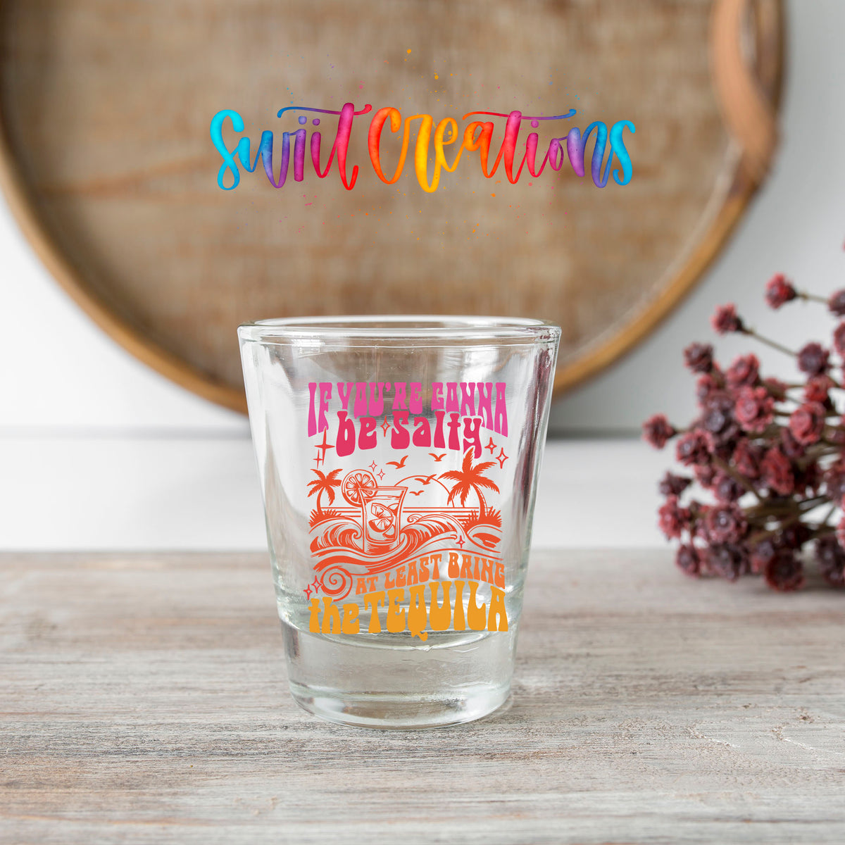 If You're Gonna Be Salty shot glass transfer on a clear glass beside a wooden barrel and dried flowers