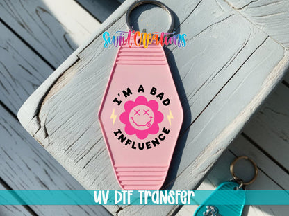 I'm a Bad Influence UV DTF transfer on a pink motel keychain on a wood board