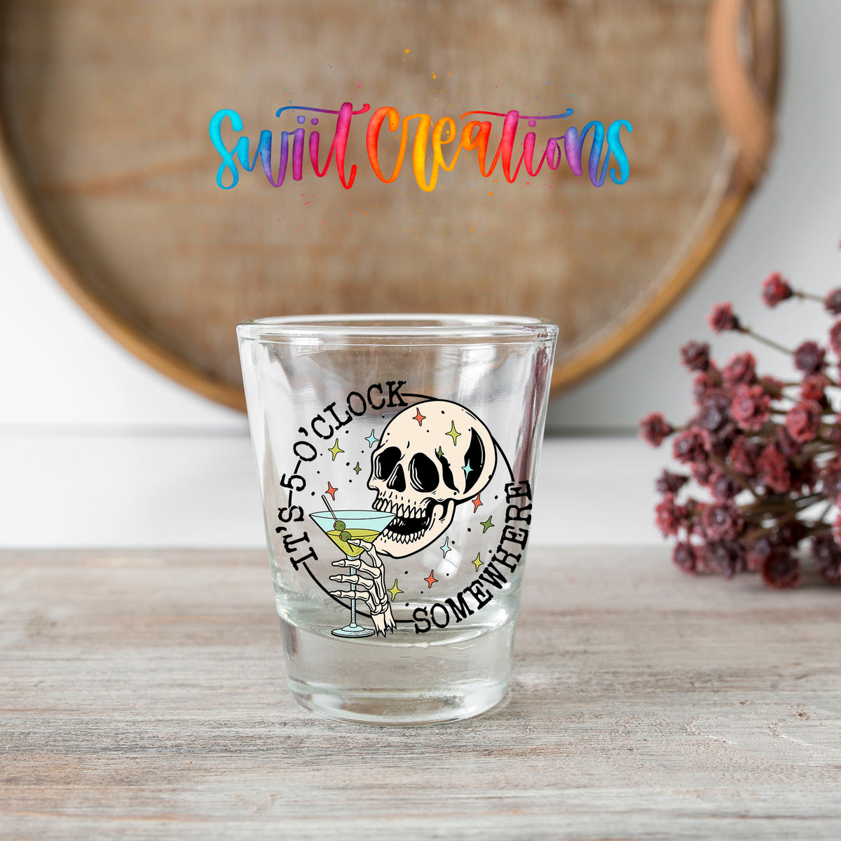 It's 5 O'Clock Somewhere shot glass transfer on a clear glass beside a wooden barrel and dried flowers