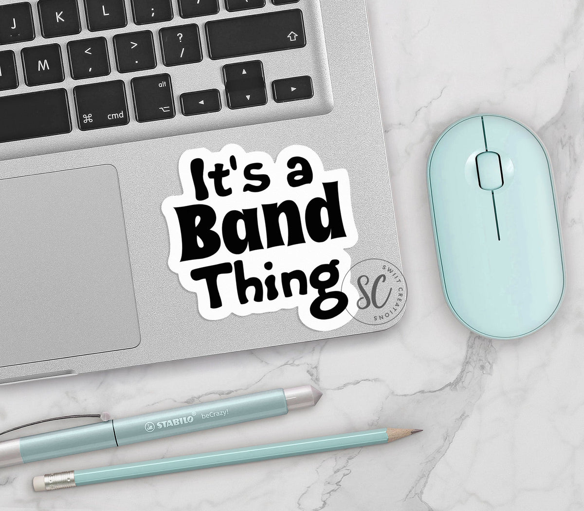 Black It's a Band Thing vinyl sticker on a silver laptop next to a mint mouse and pens