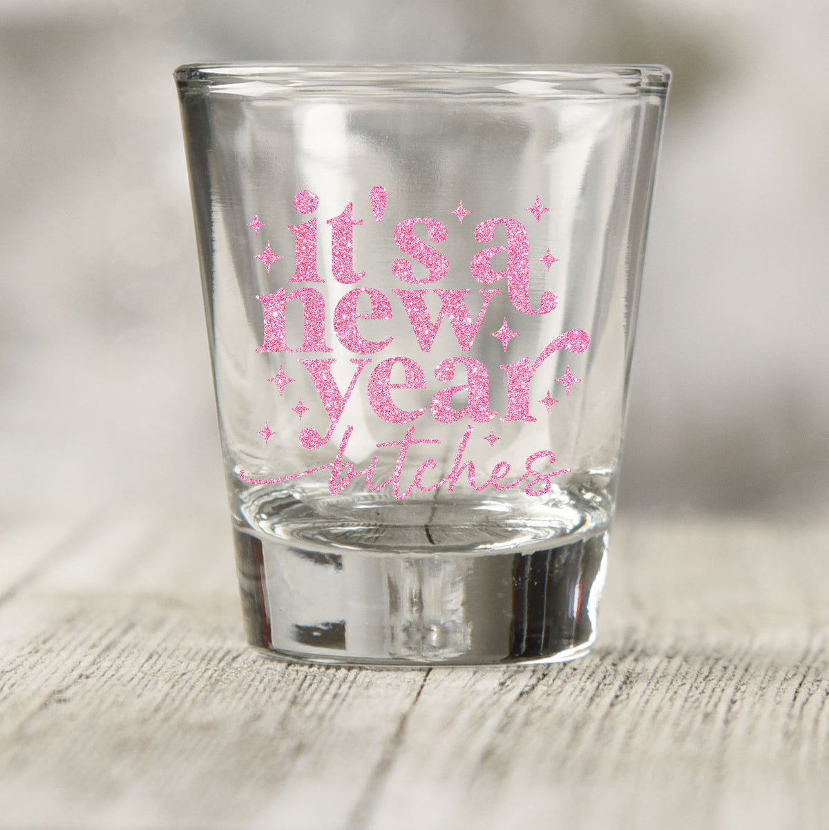 It's A New Year B*tches shot glass UV DTF transfer with pink glitter-style lettering with sparkles on a clear shot glass