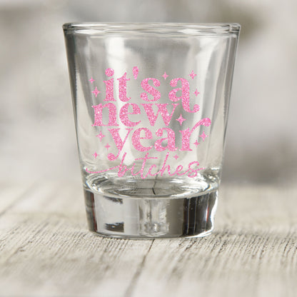 It's A New Year B*tches shot glass UV DTF transfer with pink glitter-style lettering with sparkles on a clear shot glass