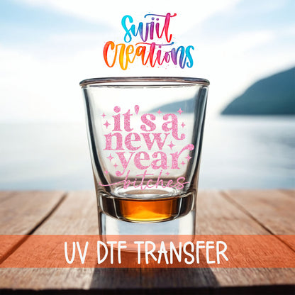 It's A New Year B*tches shot glass UV DTF transfer on a filled shot glass on a dock by the water