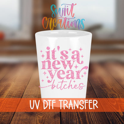 It's A New Year B*tches shot glass transfer on a white shot glass on a wooden table