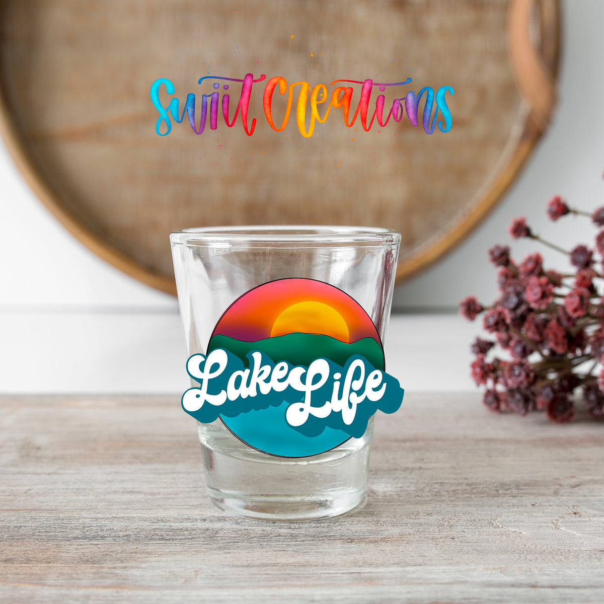 Lake Life shot glass transfer on a clear glass beside a wooden barrel and dried flowers